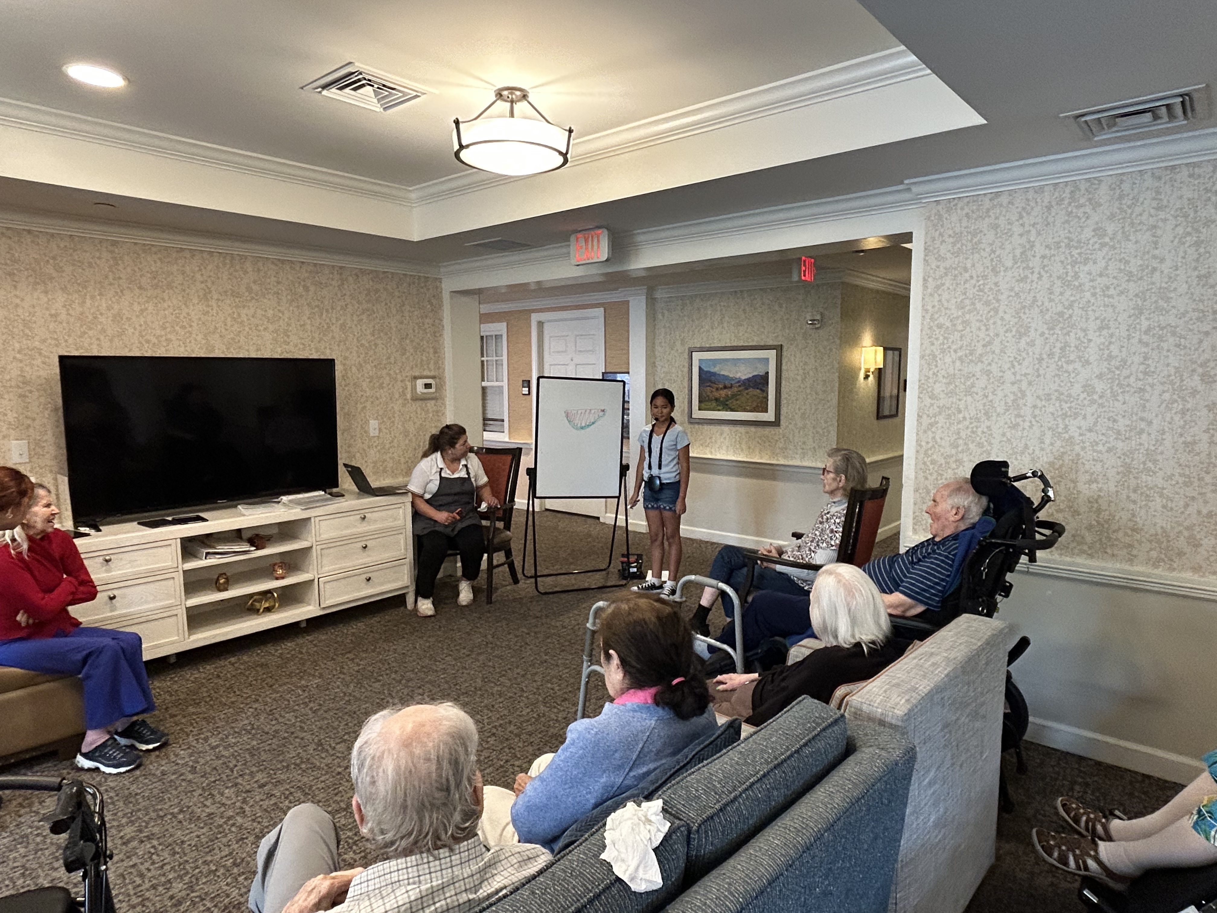 Group of memory care residents smiling while playing Pictionary with young volunteers at Sunrise Senior Living.