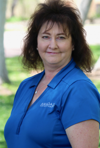 A woman dressed in a blue Amada uniform poses for the camera outside.