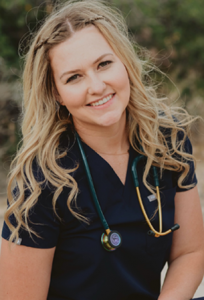 A woman in an Amanda uniform with a stethoscope around her neck smiles for the camera outside.