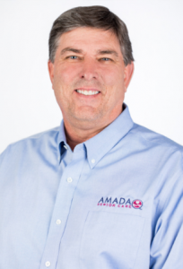 Ty Tippet_website A man in front of a white background wearing an Amada uniform smiling