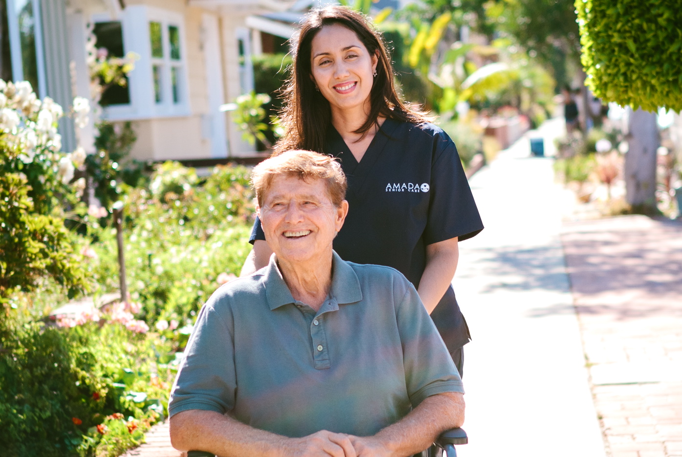 An Amada caregiver assists an elderly man on the sidewalk.