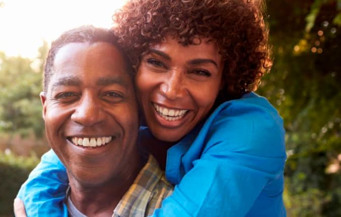 A man and a woman cuddling and smiling for the camera outside.