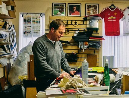 A man in gray long sleeves works at his crowded office desk.