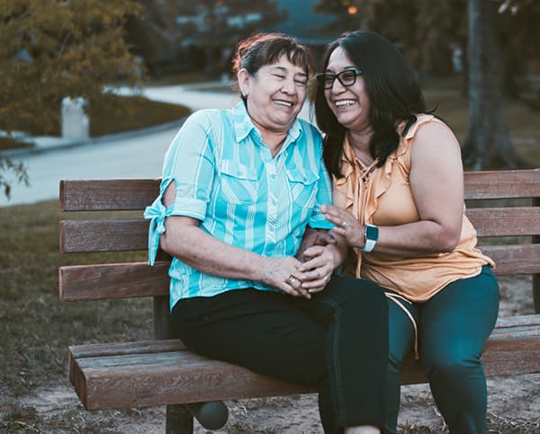 Two elderly ladies chatting and laughing on an outdoor bench.