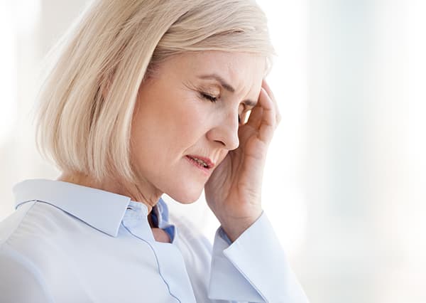 A close-up of a blonde woman holding one side of her head in pain.